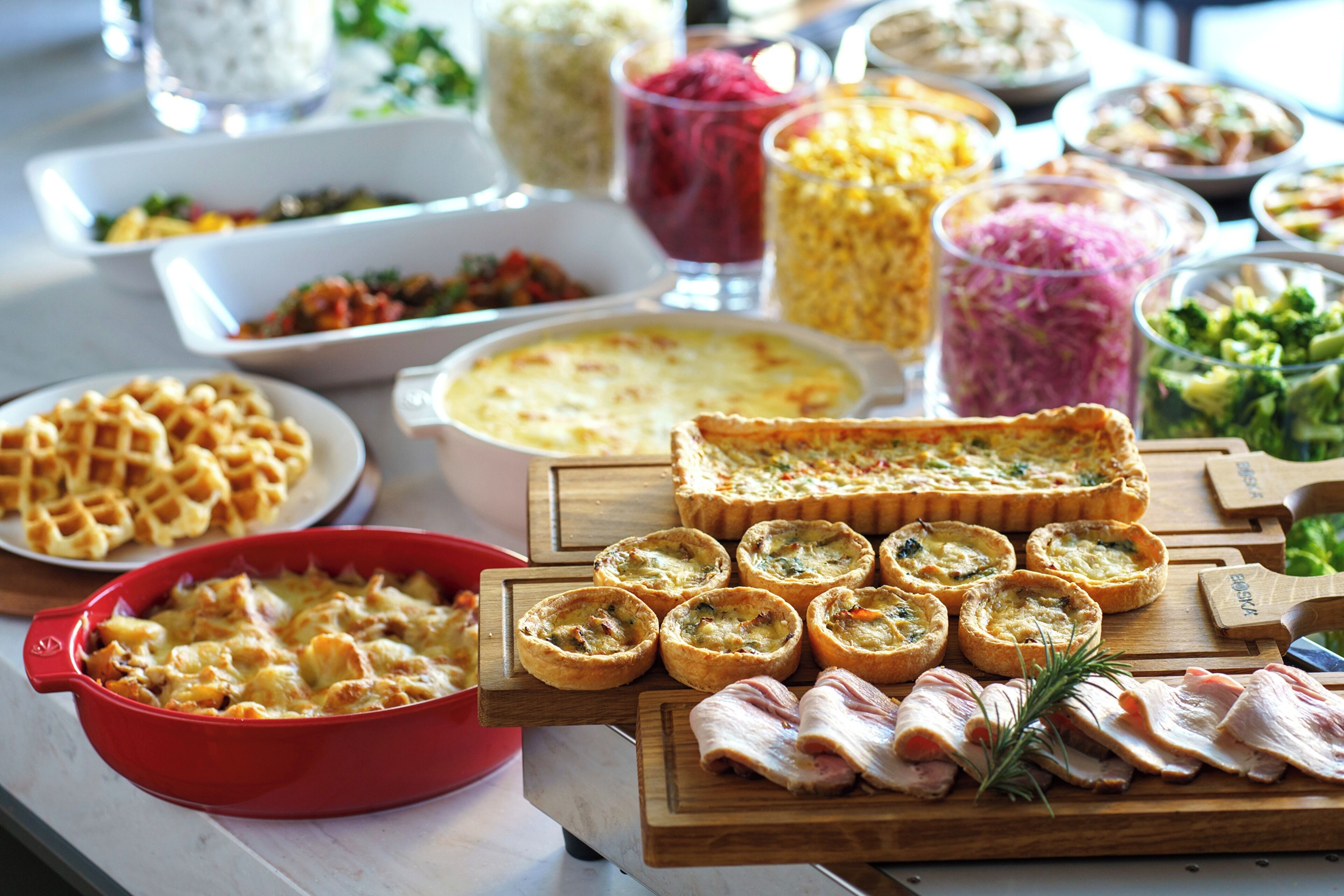 A buffet table with various dishes including waffles, quiches, and a selection of meats.