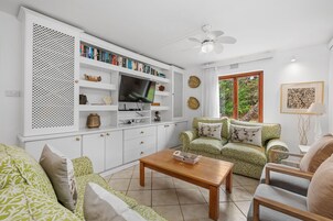 A living room with a TV, bookshelves, a green patterned sofa, and a wooden coffee table.