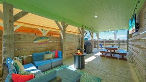 An outdoor patio with a covered seating area, a fire pit, and picnic tables. - Near the Beach, Private Pool w/ Free Heat, Firepit | Laid Back Lime by AvantStay (Port Aransas)