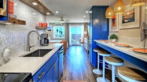 Une cuisine moderne dotée d’un îlot central, de meubles bleus et de luminaires suspendus.