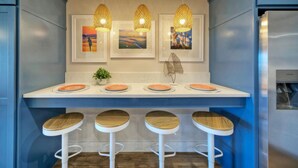 Une cuisine moderne avec un plan de travail blanc, quatre tabourets en bois et trois lampes suspendues.