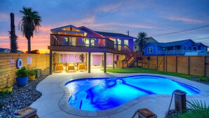A two-story house with a swimming pool, wooden deck, and a fenced backyard. - Barefoot & Salty by AvantStay | Private Pool (Port Aransas)