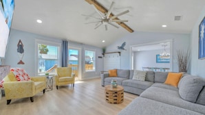 A spacious living room with a large gray sectional sofa, a yellow armchair, and a wooden coffee table. - Barefoot & Salty by AvantStay | Private Pool (Port Aransas)