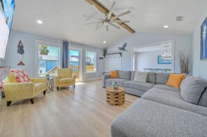 Uma sala de estar ampla com um sofá modular cinzento grande, uma poltrona amarela e uma mesa de centro de madeira.