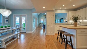 A spacious kitchen with wooden flooring, a large island with stools, and a view to the outside.