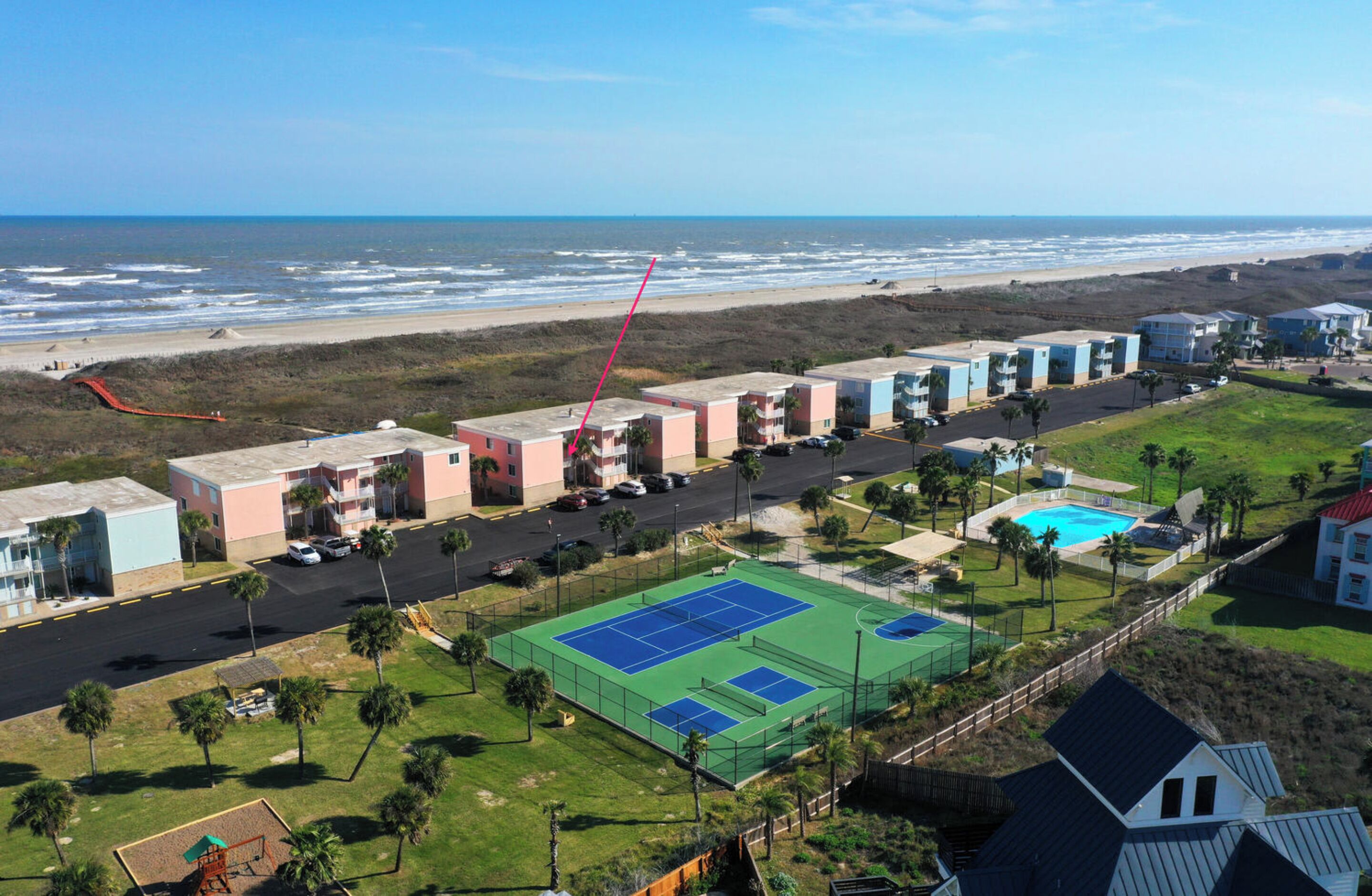 Ein Strandhotel mit mehreren Gebäuden, einem Tennisplatz und einem Swimmingpool.