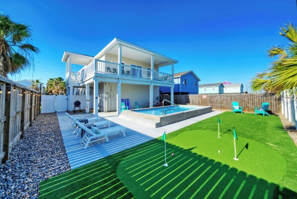 Ein zweistöckiges Haus mit Balkon, Schwimmbad und Garten mit Kunstgrasanlage und Putting Green.