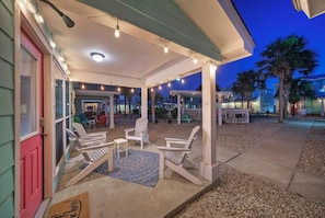 A covered outdoor area with Adirondack chairs, a concrete floor, and a door with a doormat.