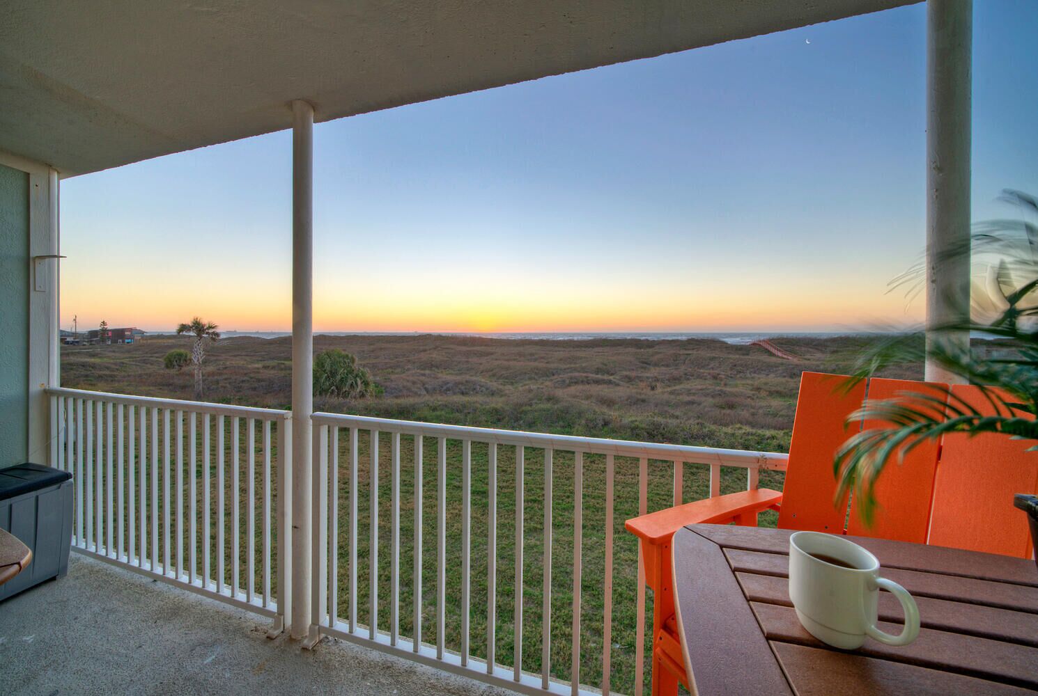 A balcony with a view of a grassy landscape and a sunset.