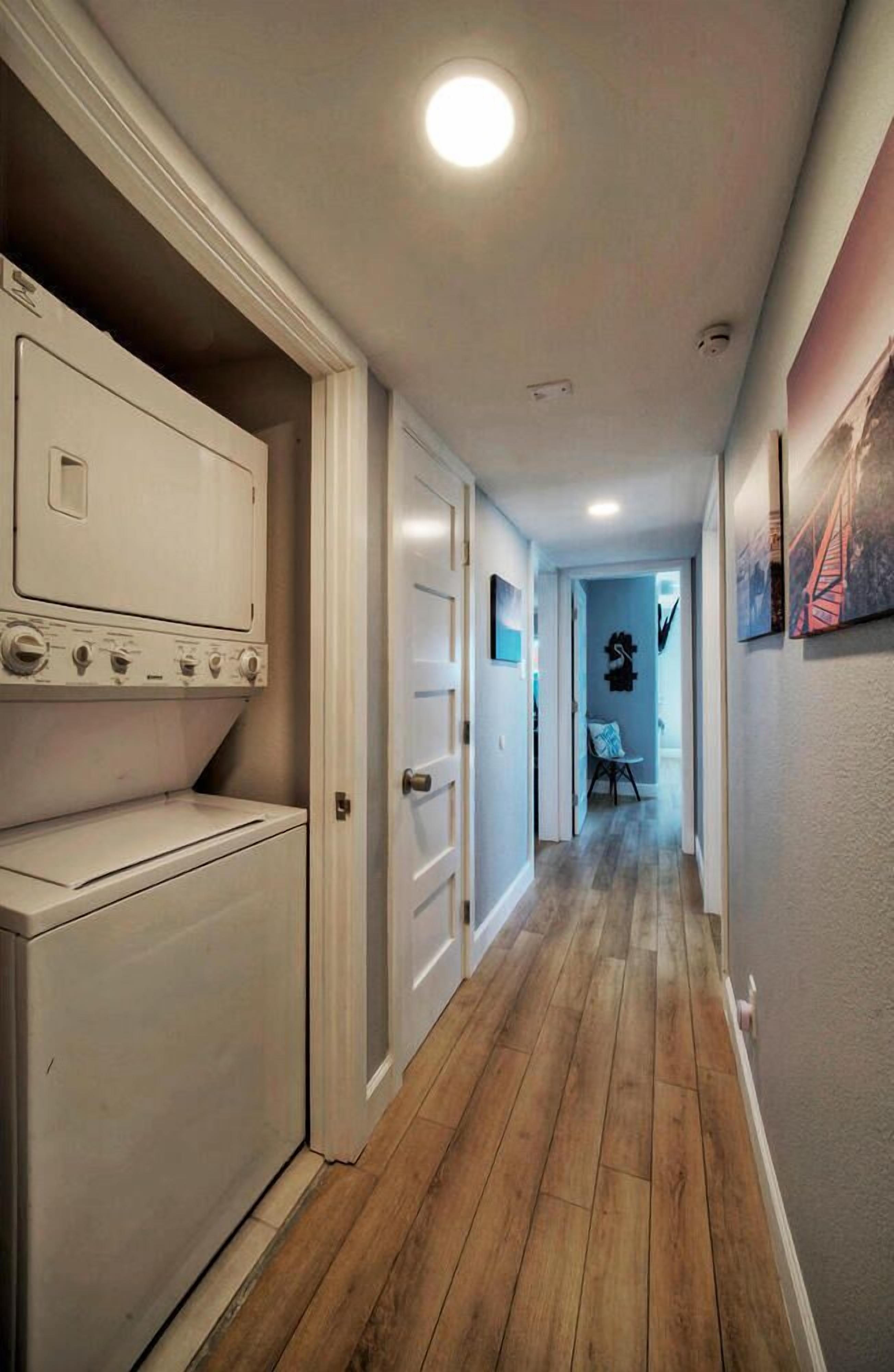 Un pasillo estrecho con un lavadero a la izquierda, suelo de madera y una puerta que da a otra habitación.