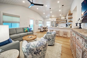 A spacious living room with a gray sofa, two patterned armchairs, a wooden coffee table, and a kitchen in the background. - Boujee Pelican by AvantStay | Pool+Game Room+Views (Port Aransas)