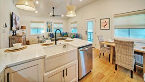 A modern kitchen with a central island, stainless steel appliances, and a dining area with wicker chairs. - Boujee Pelican by AvantStay | Pool+Game Room+Views (Port Aransas)