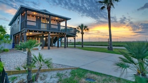 A two-story house with a balcony, a covered patio, and a view of the sunset. - Boujee Pelican by AvantStay | Pool+Game Room+Views (Port Aransas)