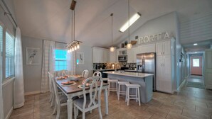 Et moderne køkken med hvide skabe, en central ø med barstole, hængende lamper og et rustfrit stål køleskab.