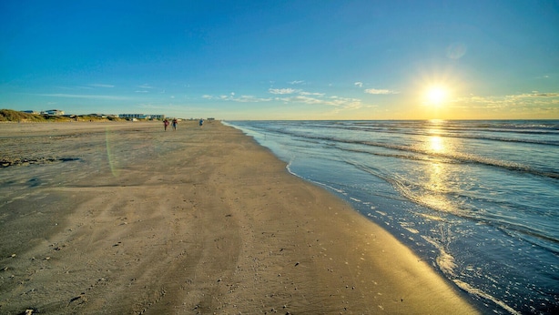 A beach with a clear sky, the sun setting or rising, and footprints in the sand. - Beachfront Condo + 2 Pools + Pickleball | Steps to Beach | Cravin' Waves (Port Aransas)