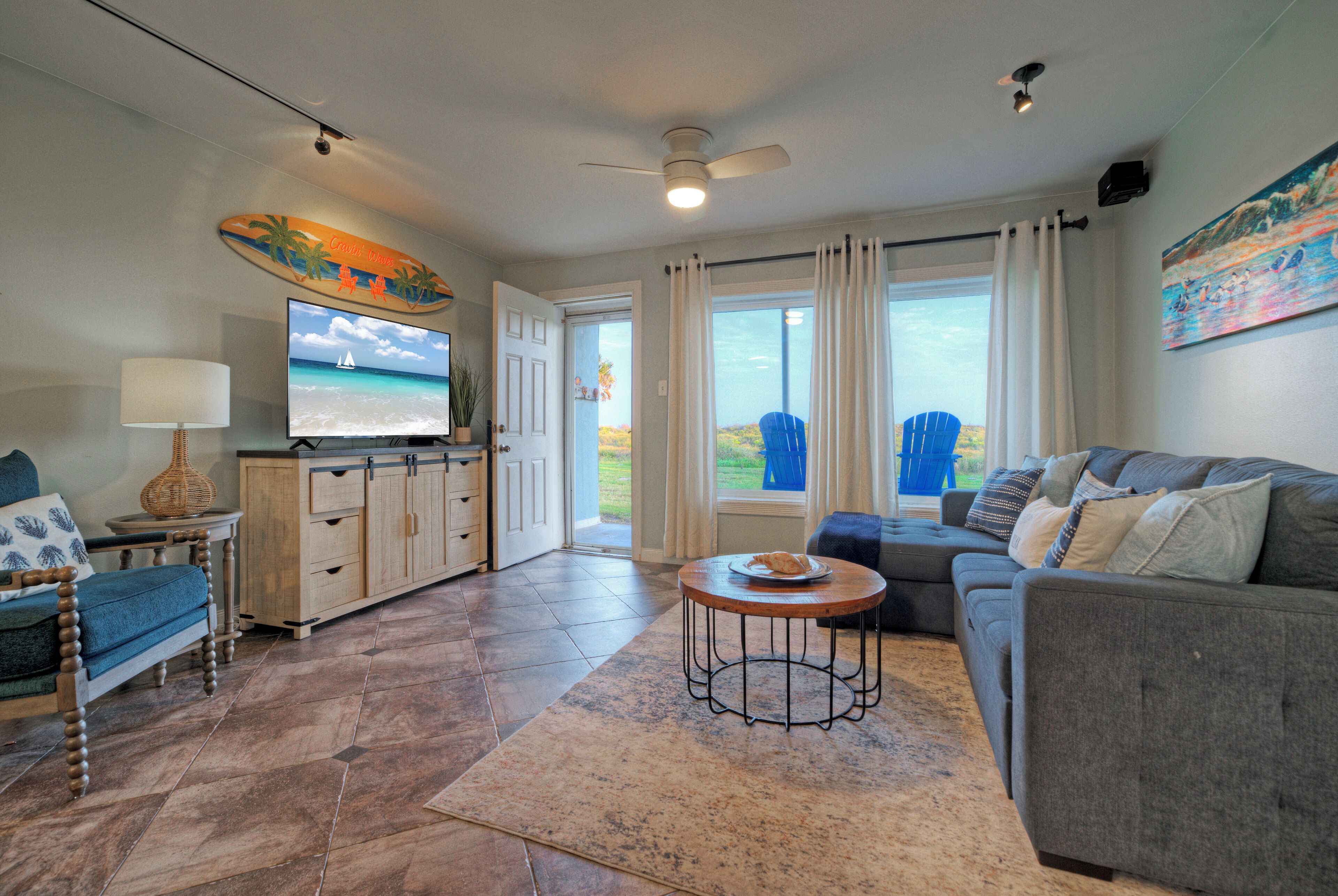 A living room with a sofa, a television, a coffee table, and a view of the outdoors.