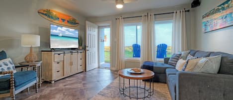 A living room with a sofa, a television, a coffee table, and a view of the outdoors.