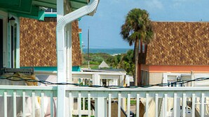 A coastal view with a white fence, a palm tree, and a building with a brown exterior. - Sun Beach by AvantStay | Private Pool, Near Beach (Port Aransas)