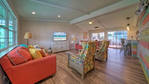 A spacious living room with a red sofa, colorful armchairs, a TV, and a view of the outdoors. - Sun Beach by AvantStay | Private Pool, Near Beach (Port Aransas)