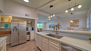A modern kitchen with white cabinetry, stainless steel appliances, and a large island with a sink. - Sun Beach by AvantStay | Private Pool, Near Beach (Port Aransas)