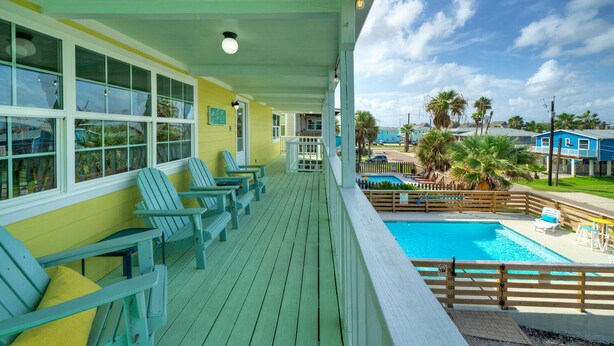 A covered porch with Adirondack chairs, a pool, and a view of the surrounding area. - Sun Beach by AvantStay | Private Pool, Near Beach (Port Aransas)