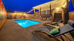 Un giardino sul retro con piscina, sedie a sdraio e zona barbecue.