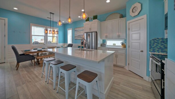 Una cucina moderna con isola centrale, sgabelli da bar, illuminazione a sospensione e un'ampia finestra.