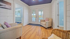 A cozy room with wooden flooring, a chair, a wicker sofa, and a door leading to an outdoor area.