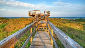 A wooden boardwalk leading to a wooden structure with a view of the ocean.