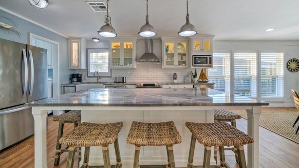 A modern kitchen with a large island, stainless steel appliances, and wicker bar stools.