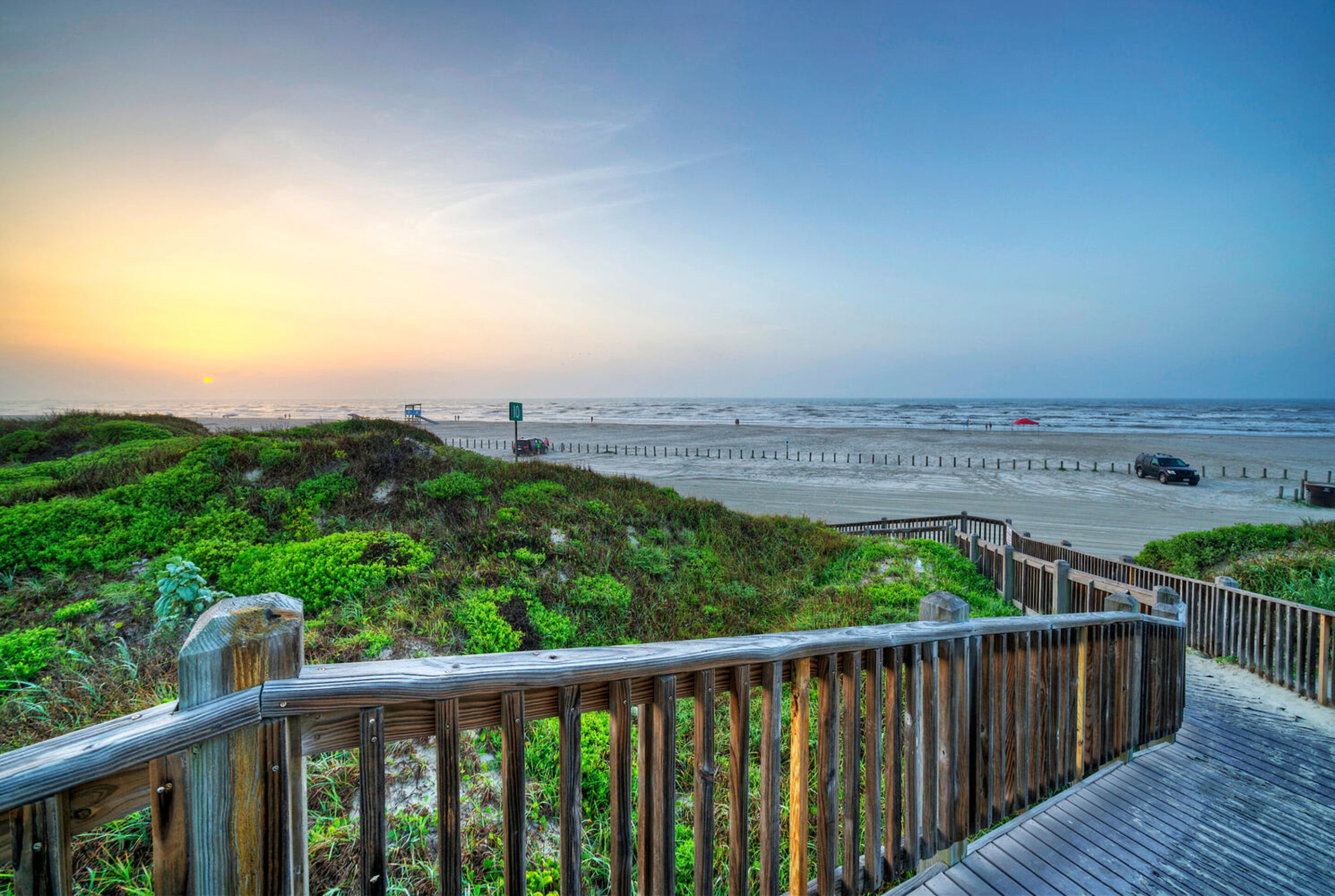 A wooden boardwalk leading to a beach with a sunset in the background.