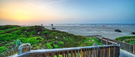 A wooden boardwalk leading to a beach with a sunset in the background.