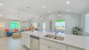 A modern kitchen with white cabinetry, a large island with a sink, and a ceiling fan. - Priv Pool, Covered Patio Lounge w/ Bar, Sunset Views | Green Gecko by AvantStay (Port Aransas)