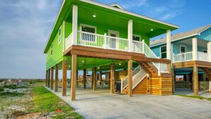 A two-story house with a green exterior and a wooden deck. - Priv Pool, Covered Patio Lounge w/ Bar, Sunset Views | Green Gecko by AvantStay (Port Aransas)
