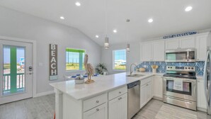 A modern kitchen with white cabinetry, stainless steel appliances, and a large island. - Priv Pool, Covered Patio Lounge w/ Bar, Sunset Views | Green Gecko by AvantStay (Port Aransas)