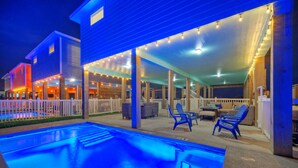 A pool area with a covered patio, lounge chairs, and a view of adjacent buildings.