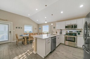 Una cocina moderna con armarios blancos, electrodomésticos de acero inoxidable y un comedor con sillas y mesa de madera.