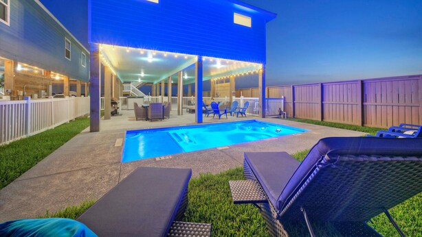 A backyard with a swimming pool, lounge chairs, and a covered patio area.