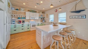 A modern kitchen with wooden cabinets, a central island with stools, and a sailboat decoration on the wall. - Fishing Pond Views + Fire Pit + Hammock Lounge + Pool | Best Little Shore House (Port Aransas)