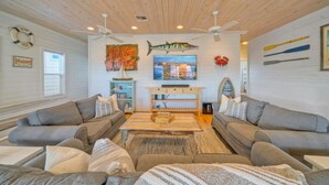A living room with two grey sofas, a wooden coffee table, a TV, and a ceiling fan. - Fishing Pond Views + Fire Pit + Hammock Lounge + Pool | Best Little Shore House (Port Aransas)