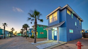 A two-story building with a blue exterior and a green door, located in a residential area with palm trees.