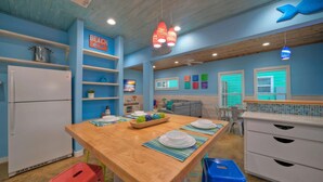 A kitchen with a wooden island, colorful stools, a refrigerator, and a sign indicating a beach direction.