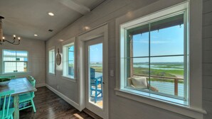 Quarto com piso de madeira, mesa de jantar com cadeiras e grandes janelas com vista para o exterior.