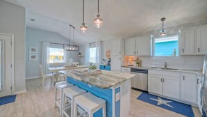 A modern kitchen with white cabinets, a blue island, and pendant lighting.