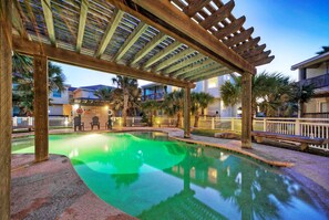 A pool area with a wooden pergola overhead, palm trees, and a building in the background. - Pool, Walkable to Old Town Eateries, Nightlife, Shops | Palm Palace by AvantStay (Port Aransas)