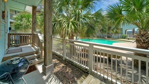 Eine Holzterrasse mit Grill, Pool und Palmen.
