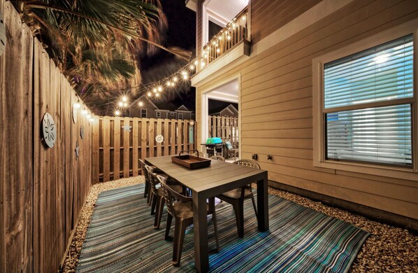 An outdoor patio with a wooden table and chairs, string lights, and a decorative fence.