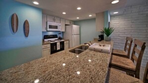 Una cocina con encimeras de granito, gabinetes blancos, microondas y refrigerador.