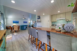 A spacious kitchen with wooden cabinets, a large island with bar stools, and a dining area with a blue sofa and wooden table. - Big Yard w/ Priv Pool, Firepit, Patio | Near the Beach | Reel Time by AvantStay (Port Aransas)