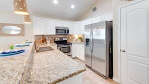 A kitchen with white cabinets, a stainless steel refrigerator, a microwave, an oven, and a sink. - Salty Peach by AvantStay | Private Pool, New Decor (Port Aransas)